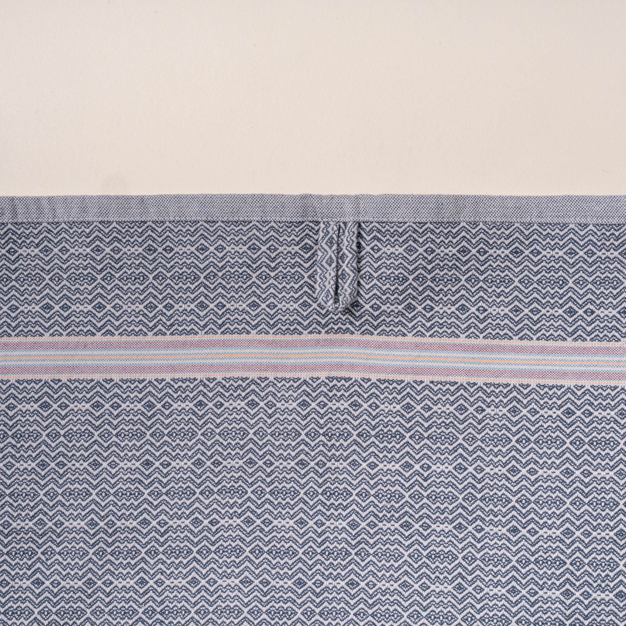 Close-up of a grey woven towel with a zigzag-and-diamond texture, stitched hanging loop, and thin striped band detail.