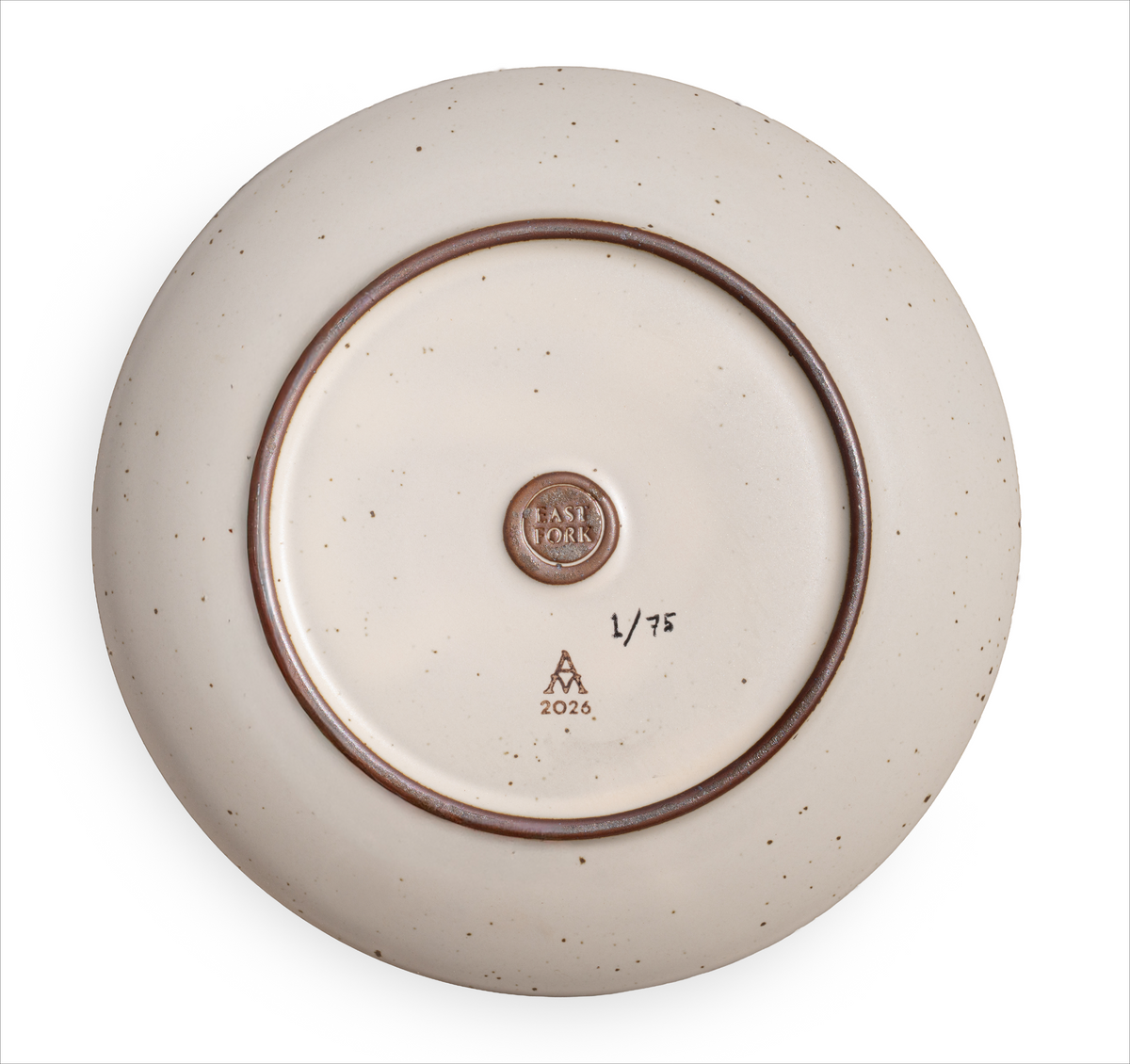 The back of a ceramic plate with iron spots in an off-white color, with a EAST FORK stamp, and an artist signature and edition of 1/75. 