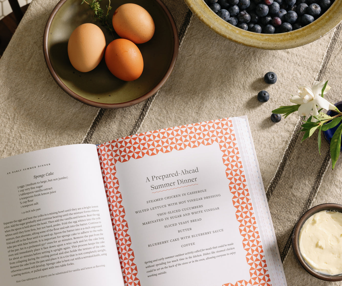 An open Taste of Country Cooking cookbook on a tablecloth with bowls of ingredients