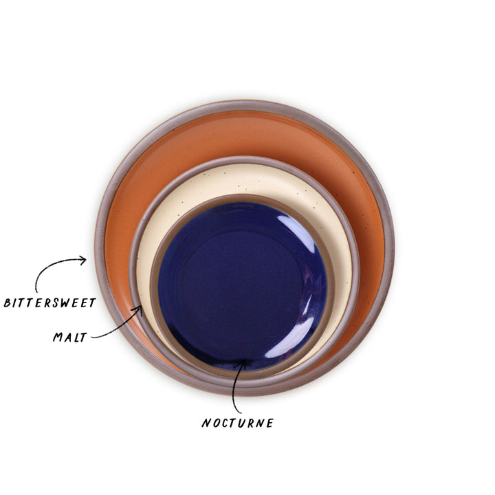 A trio of nesting plates in cream, bold orange, and glossy dark blue colors.