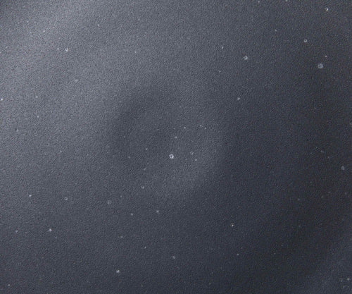 A closeup of a ceramic plate in a graphite black color with iron speckles throughout