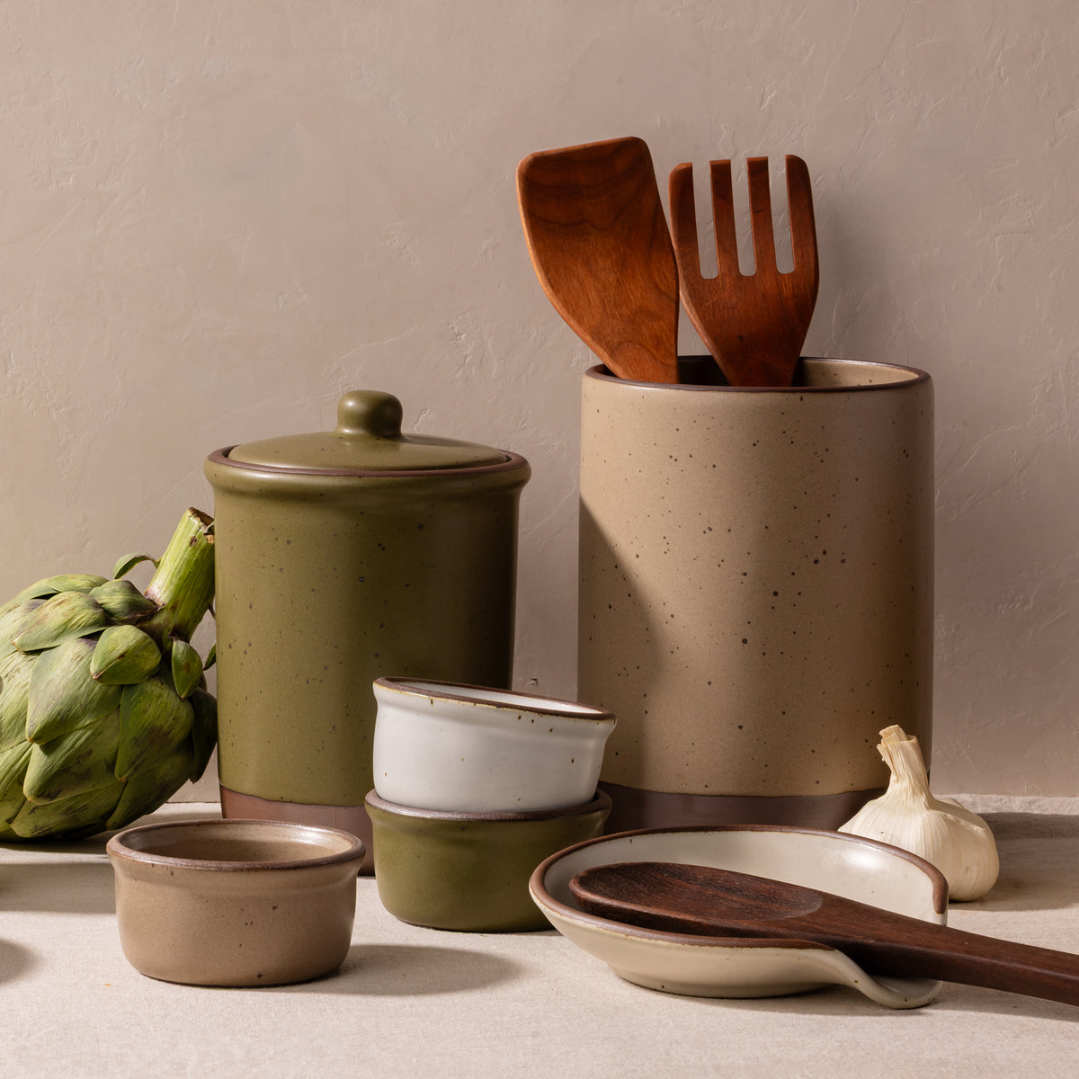 Ceramic utensil crock, tall jar, small ramekins and spoon rest with spoons and serving sets.