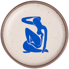 A plate featuring Nu Bleu I, by Henri Matisse, a bright blue, abstract, silhouetted female figure in a curled, seated position, with sharp cut-out edges, centered on an off-white ceramic plate with an unglazed rim.