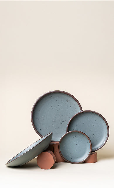 Blue-grey ceramic pottery artfully arranged with raw clay against a cream background.