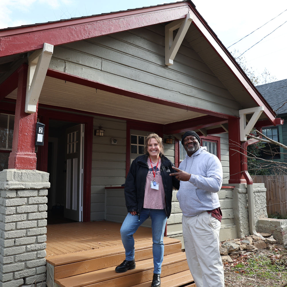 Two people standing on a porch of a small house with a red roof.