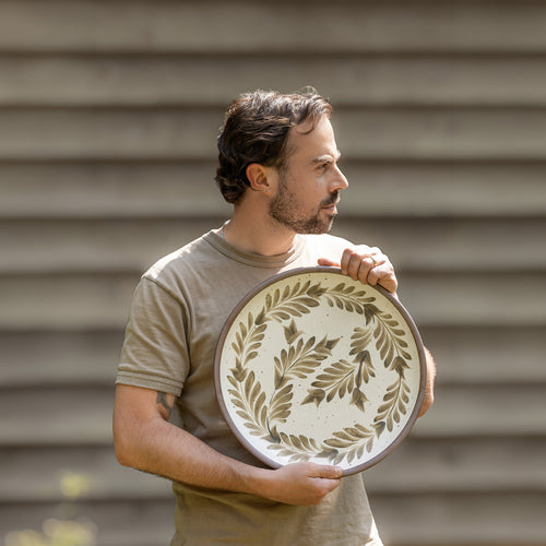 Alex outside holding a large serving platter with hand painted greenery design on it