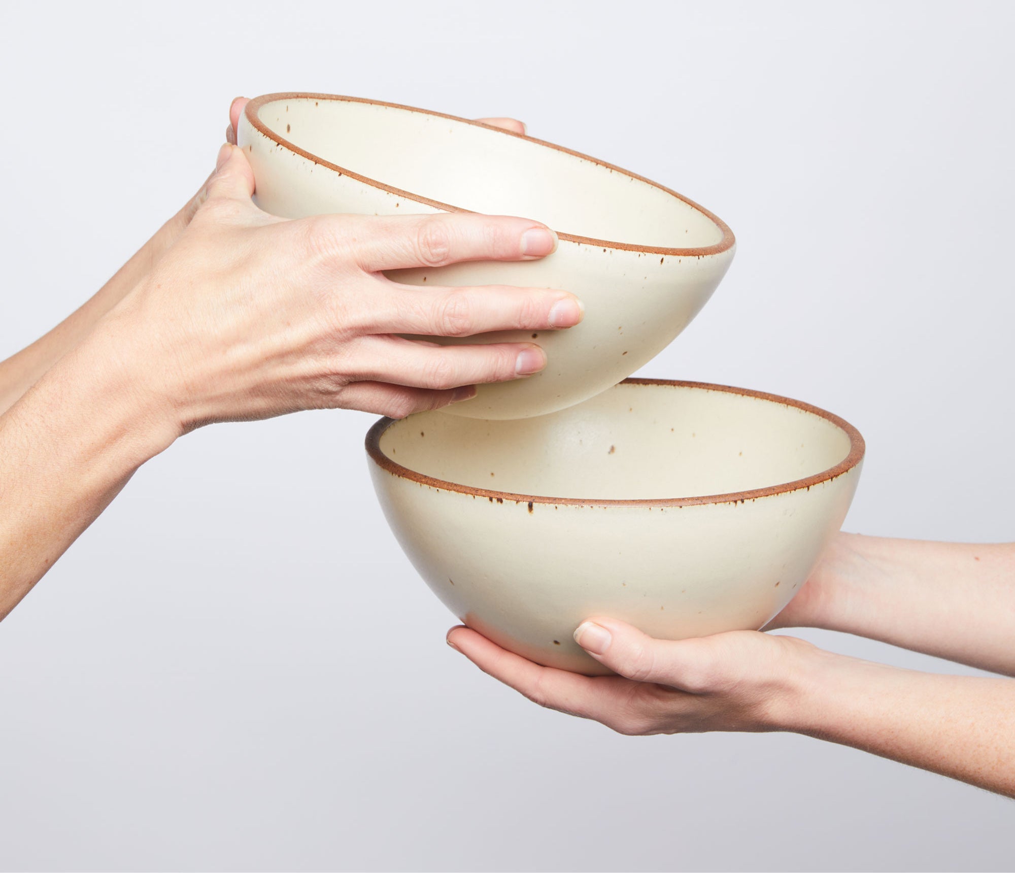 Two hands holding two ceramic bowls against a light gray background
