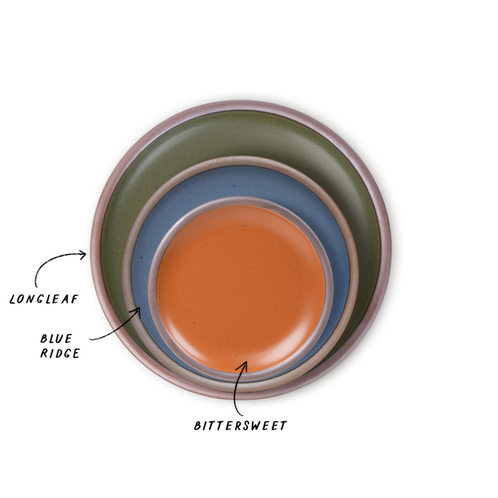 Three nested ceramic plates in a pine green, blue, and earthy orange glazes, shown from a top-down view on a white background with text labels pointing to each color