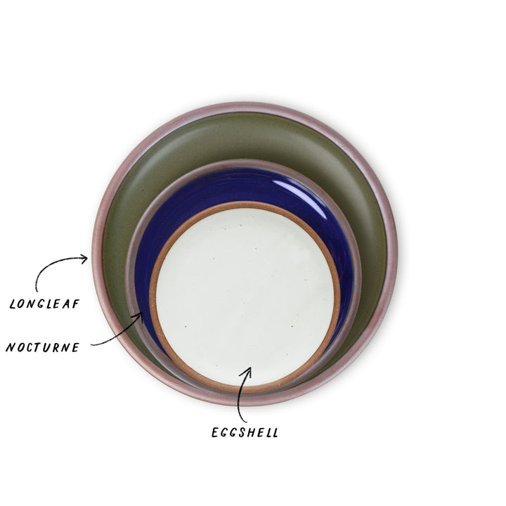 Three nested ceramic plates shown from a top-down view on a white background, with handwritten labels pointing to each: LONGLEAF in the outer pine green-toned plate, NOCTURNE in the glossy dark blue plate, and EGGSHELL in the blue-white plate. 