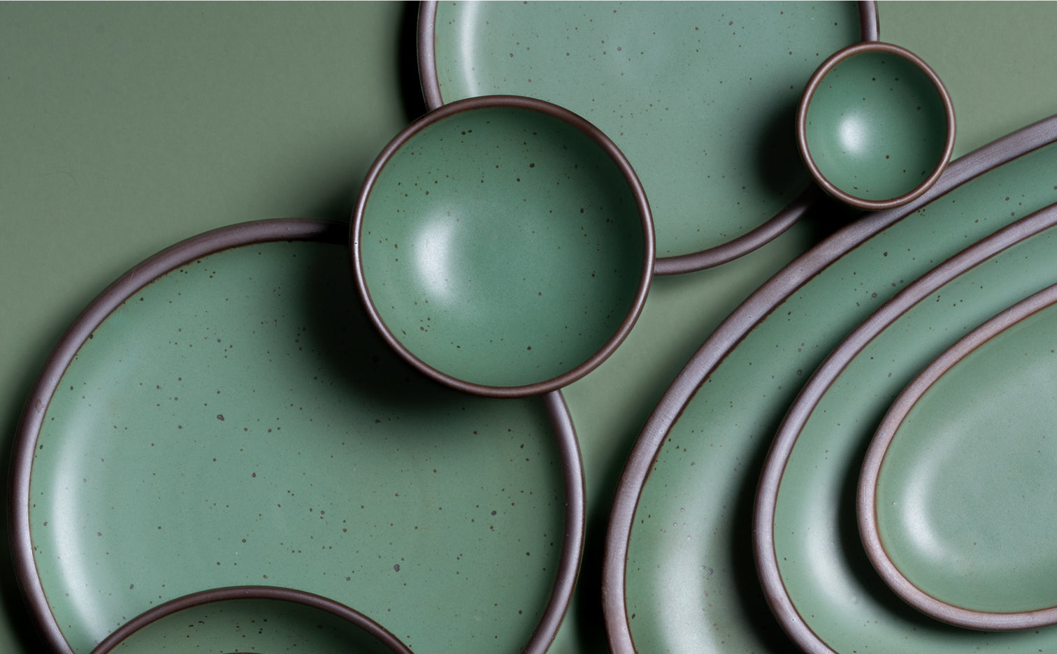 Green ceramic plates and bowls with brown rims on a green background