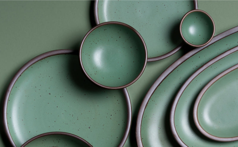 Green ceramic plates and bowls with brown rims on a green background