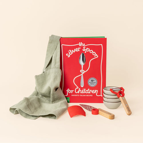 A children's cooking set featuring The Silver Spoon for Children cookbook, a sage green apron, four small ceramic bowls in a matte warm off-white color with unglazed rims, arranged against a cream background.