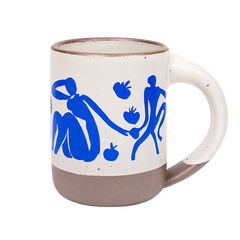 East Fork’s The Mug in a warm off white color with handle with a blue decal of Henri Matisse’s Femmes et singes, a bright blue, abstract cut-out figures of women sitting, monkeys, and pomegranate across the body of the mug