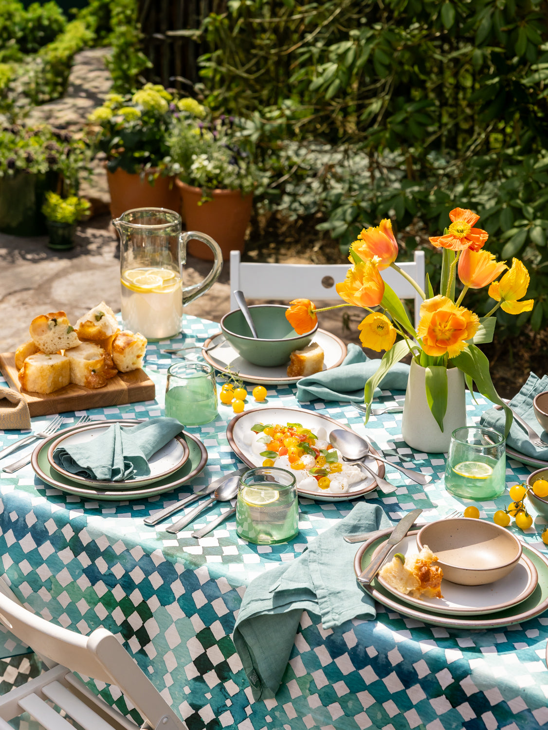 Outdoor dining table set with plates, glasses, and a vase of yellow flowers.