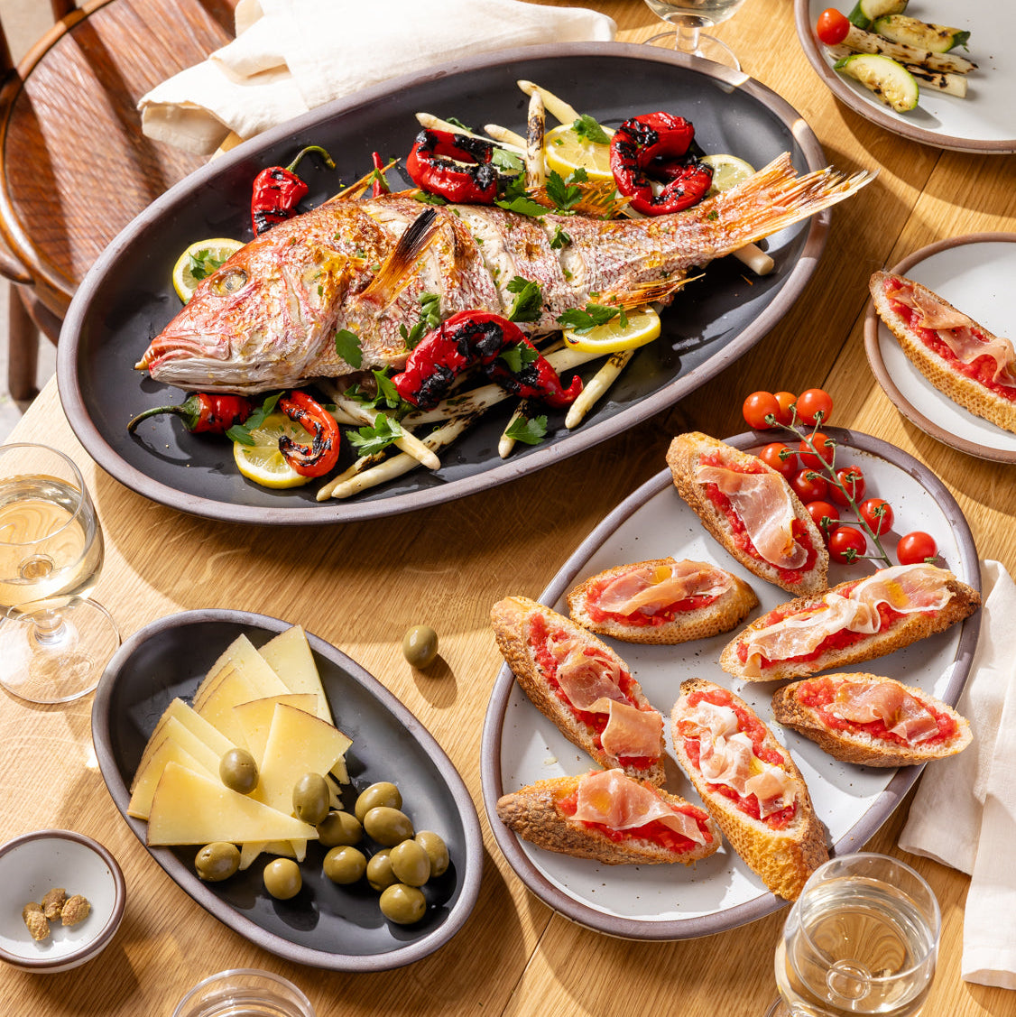 Dining table set with a roasted fish dish, bruschetta, and appetizers on a wooden table.