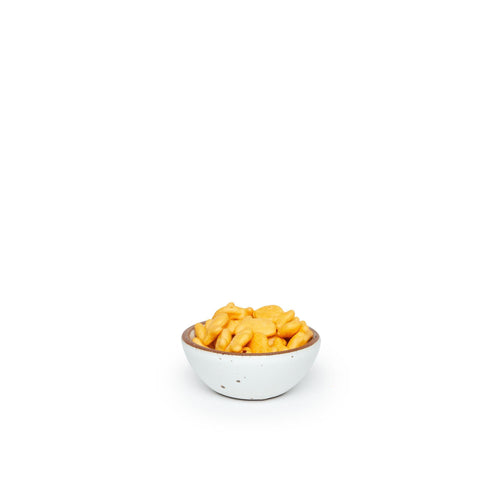 A tiny rounded ceramic bowl in a cool white color featuring iron speckles and an unglazed rim, filled with tiny crackers