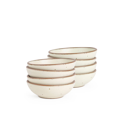 A stack of 8 small shallow ceramic bowls in a warm off-white color featuring iron speckles and an unglazed rim