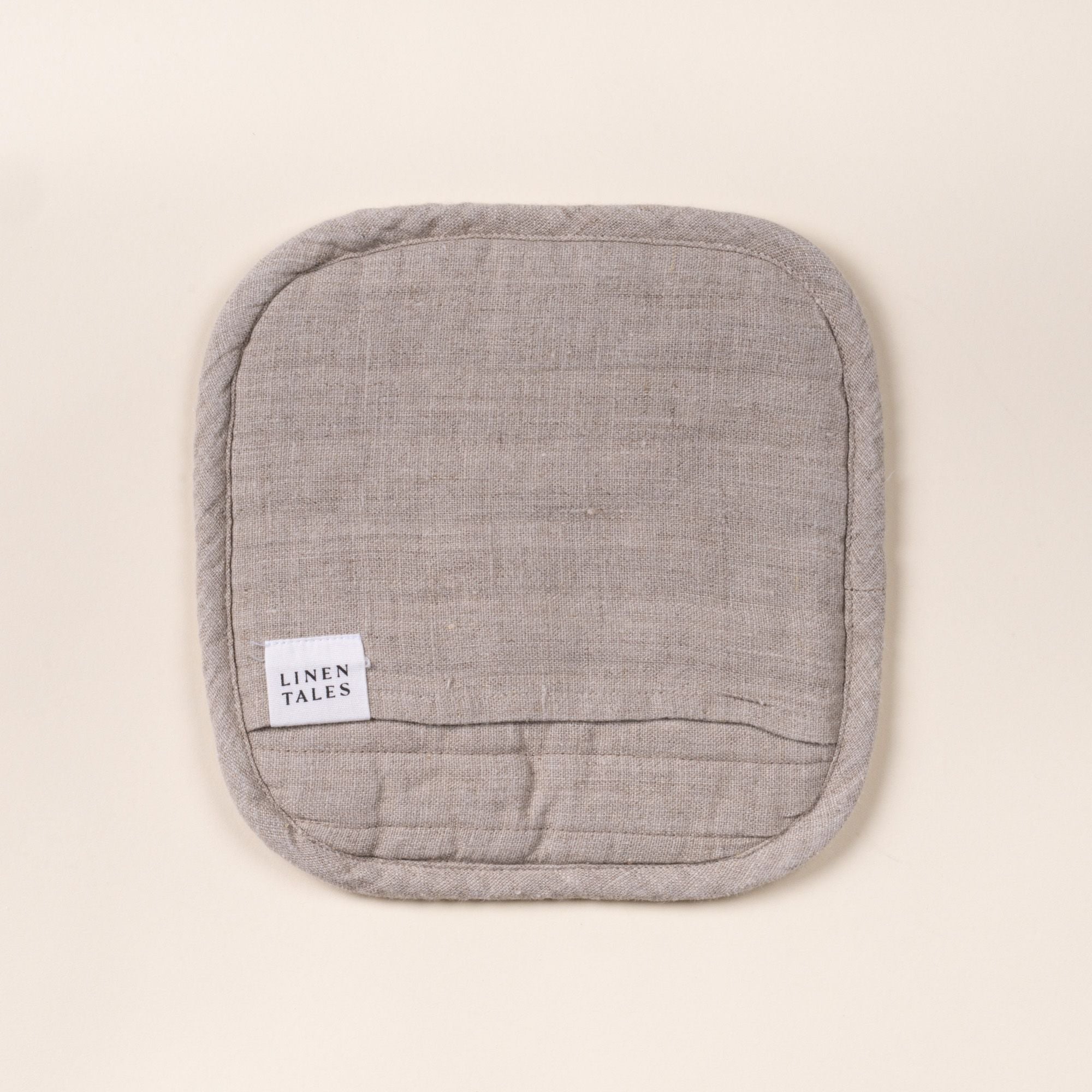 Square quilted linen potholder in a natural color with rounded corners and a small ‘LINEN TALES’ label, on a light background.