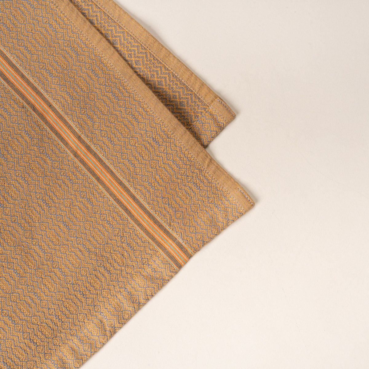 Corner of a muted gold woven kitchen towel with a subtle textured pattern and slim striped accent, folded neatly on a clean neutral background.