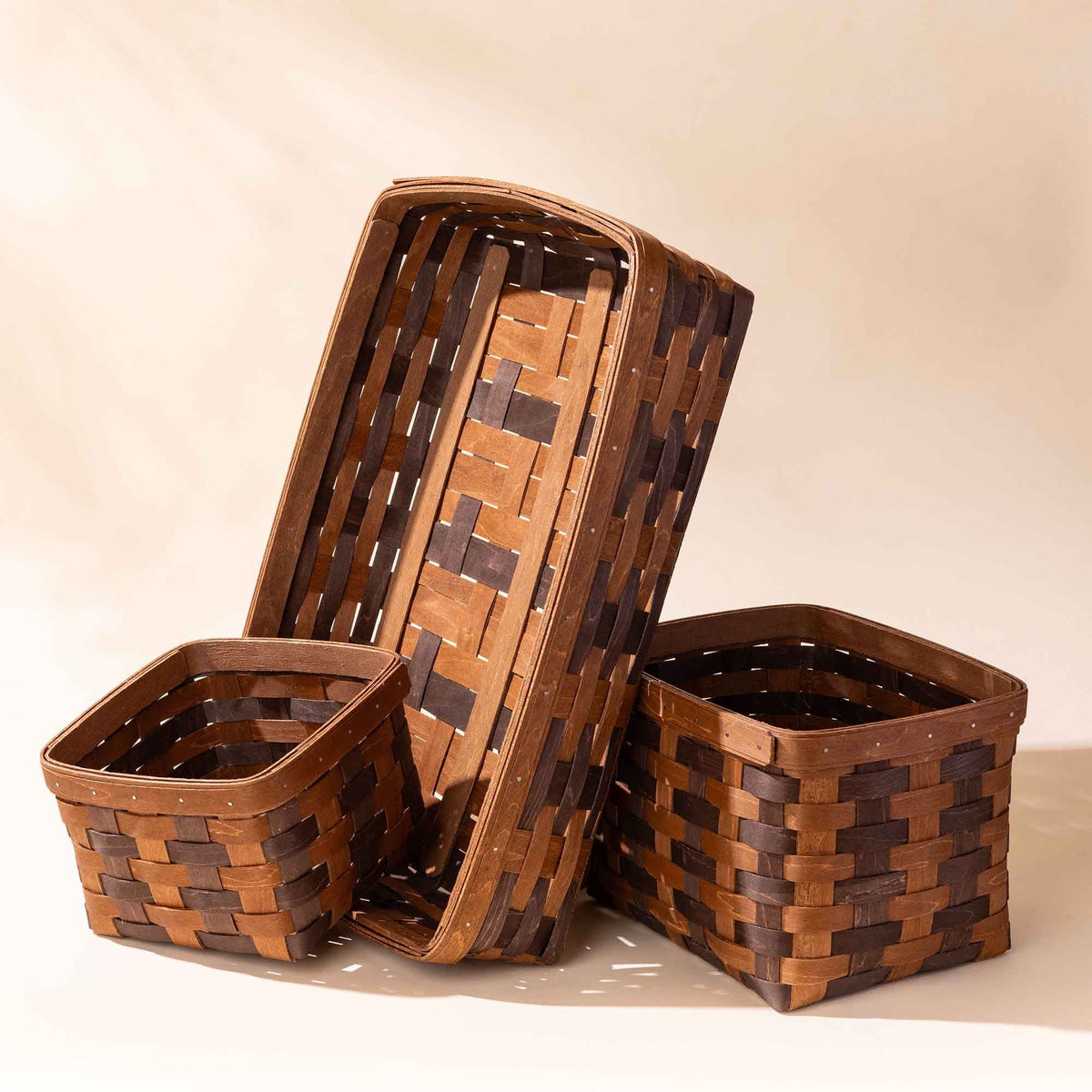 Set of three woven wooden storage baskets in different sizes with a two-tone pattern.