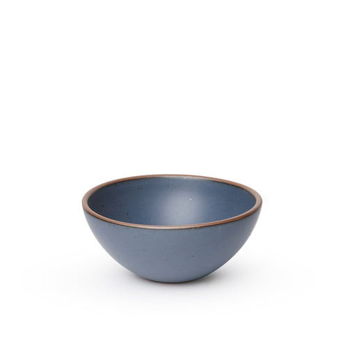 A medium rounded ceramic bowl in a cool, medium blue color featuring iron speckles and an unglazed rim