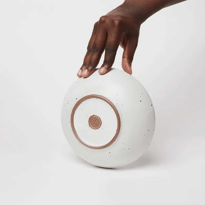 A gif of a hand holding a shallow everyday bowl, spinning it around, and then another hand placing a small shallow bowl and nestling it inside the first bowl.