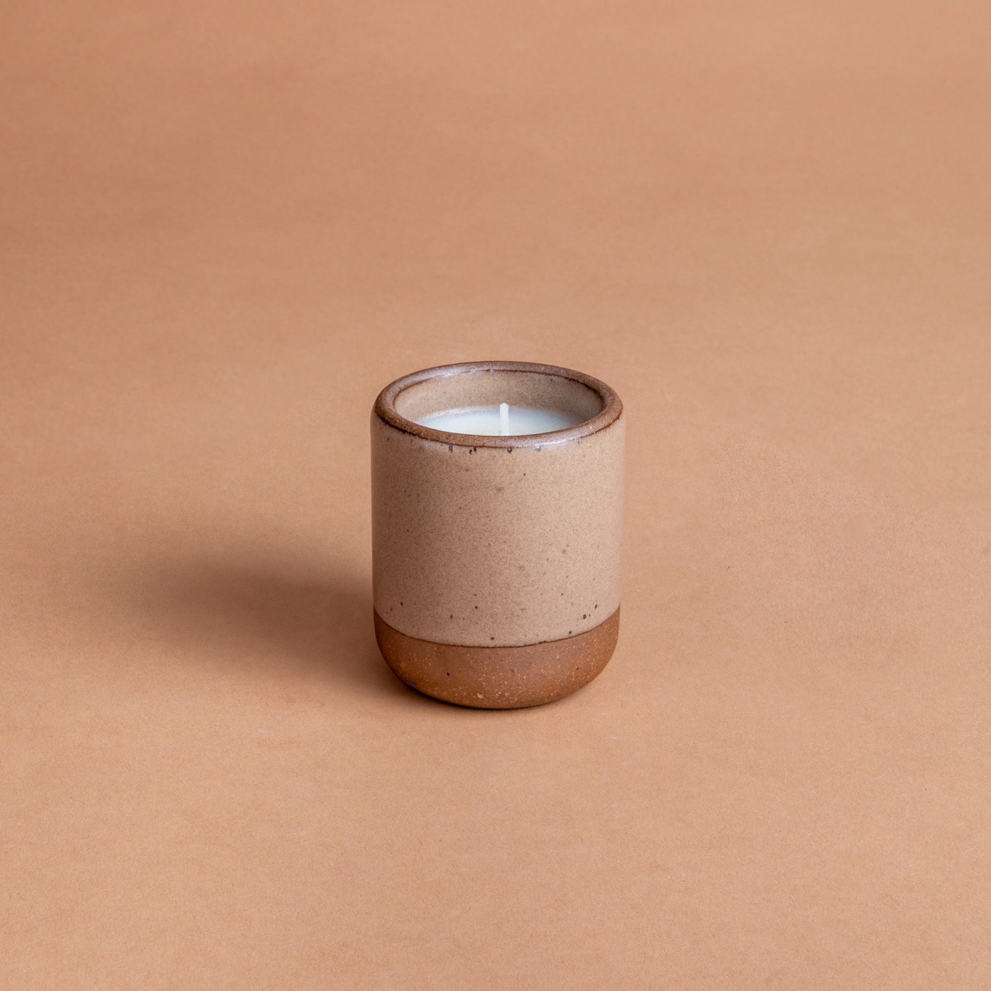 Small ceramic vessel in a warm pale brown color with candle inside.