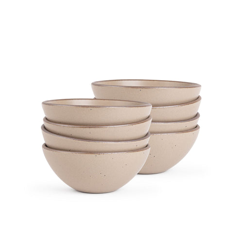 A stack of 8 medium rounded ceramic bowls in a warm pale brown color featuring iron speckles and an unglazed rim