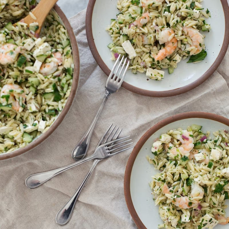 Ceramic plates in a cool white color filled with a shrimp pasta salad and silverware.