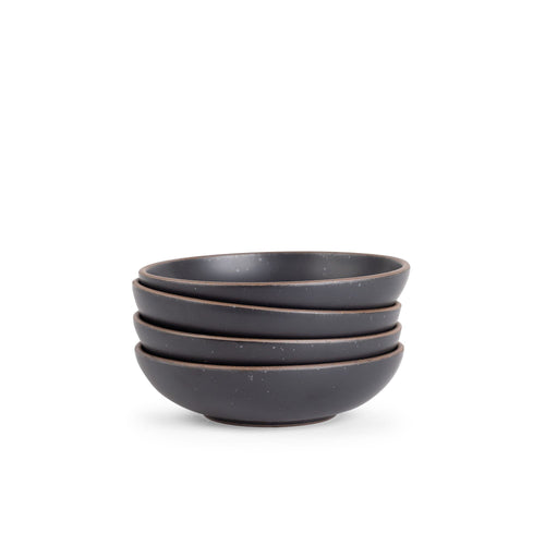 A stack of 4 dinner-sized shallow ceramic bowls in a graphite black color featuring iron speckles and an unglazed rim
