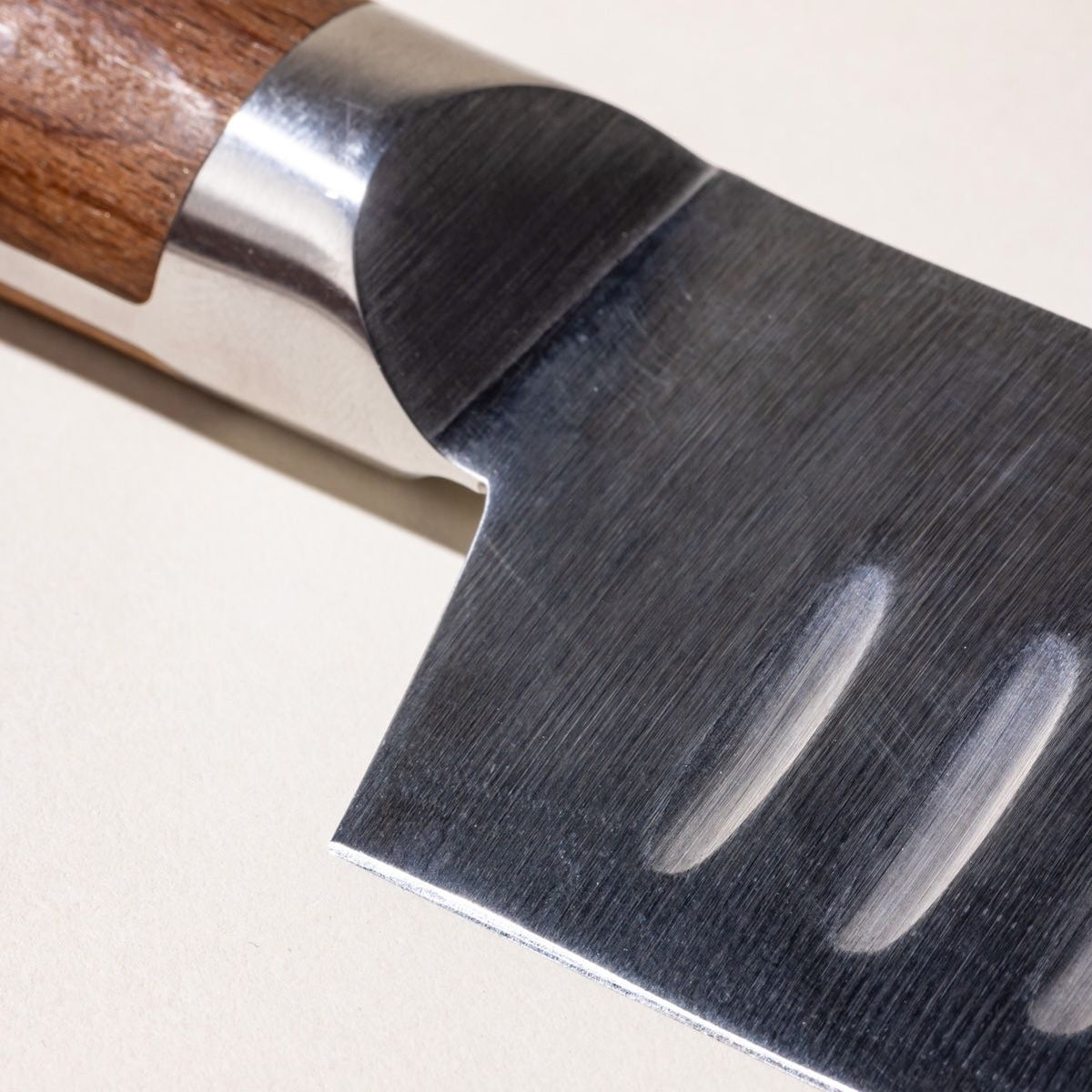 A close up of where the wooden handle meets the steel blade of a santoku knife