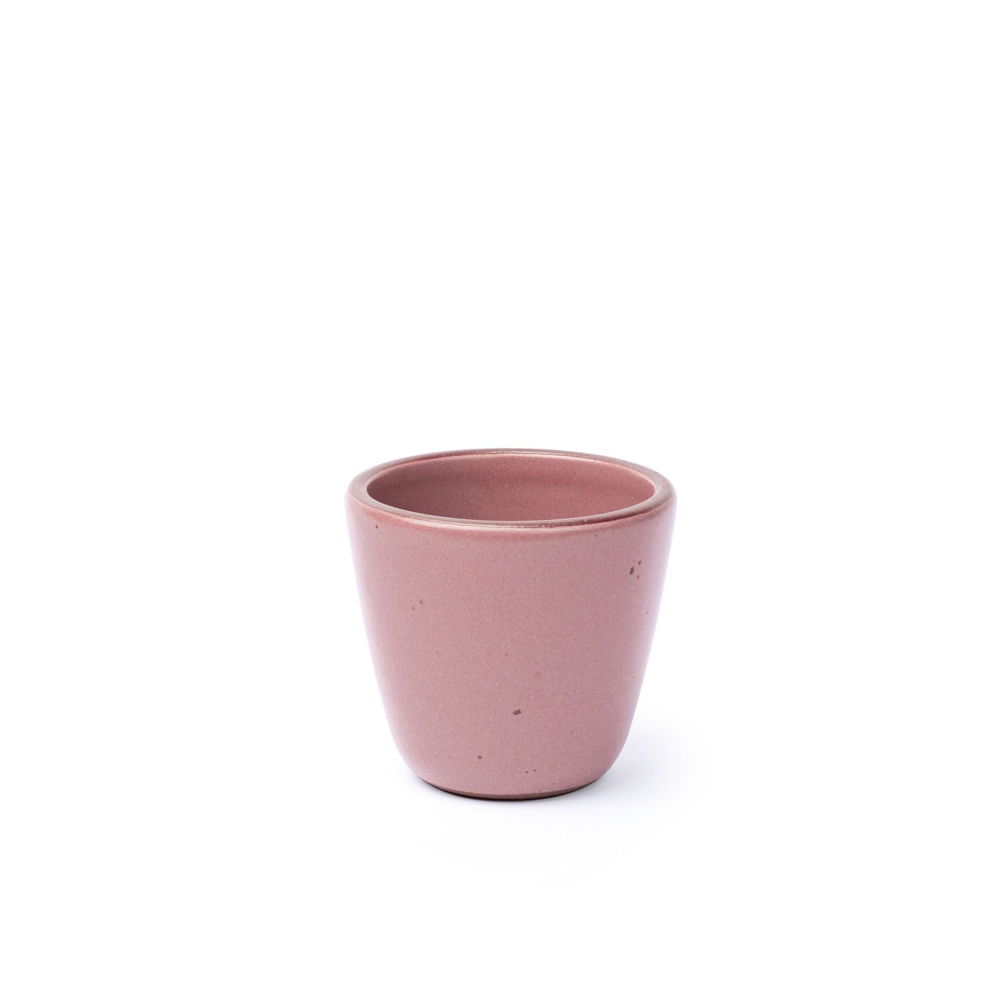 A short cup that tapers out to get wider at the top in a dusty mauve pink color featuring iron speckles