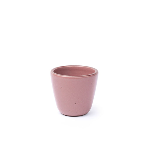A short cup that tapers out to get wider at the top in a dusty mauve pink color featuring iron speckles