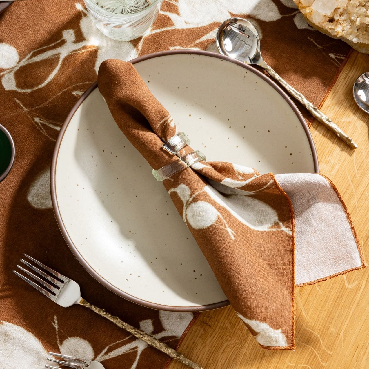 Brown and white patterned napkin with clear glass napkin ring on a white plate with silverware.