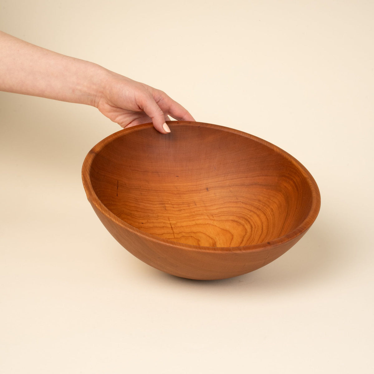 A hand holds out a large cherry wood bowl