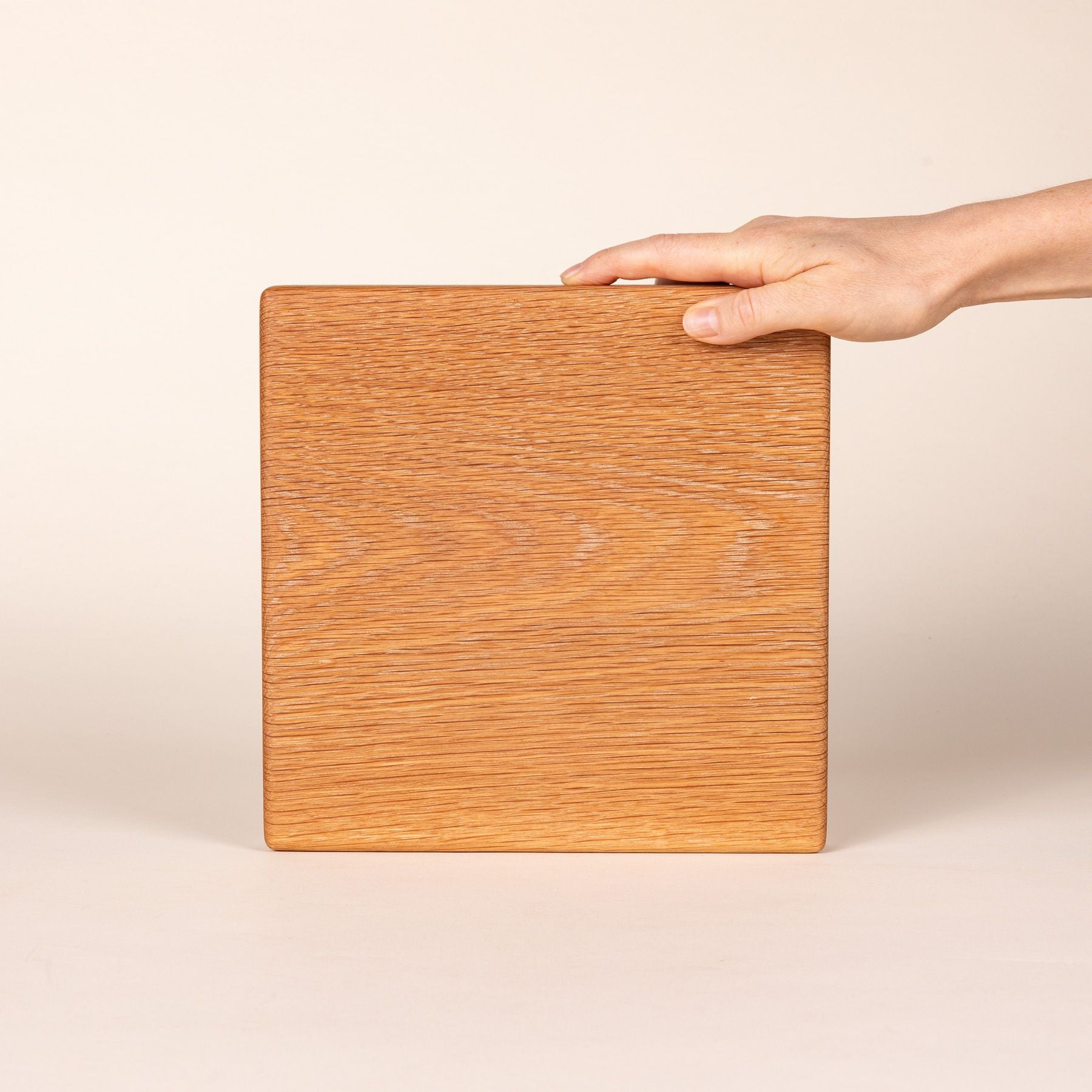 A hand props up a square white oak cutting board on its side