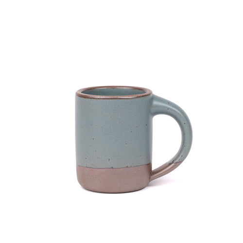 A medium sized ceramic mug with handle in a blue-grey color featuring iron speckles and unglazed rim.