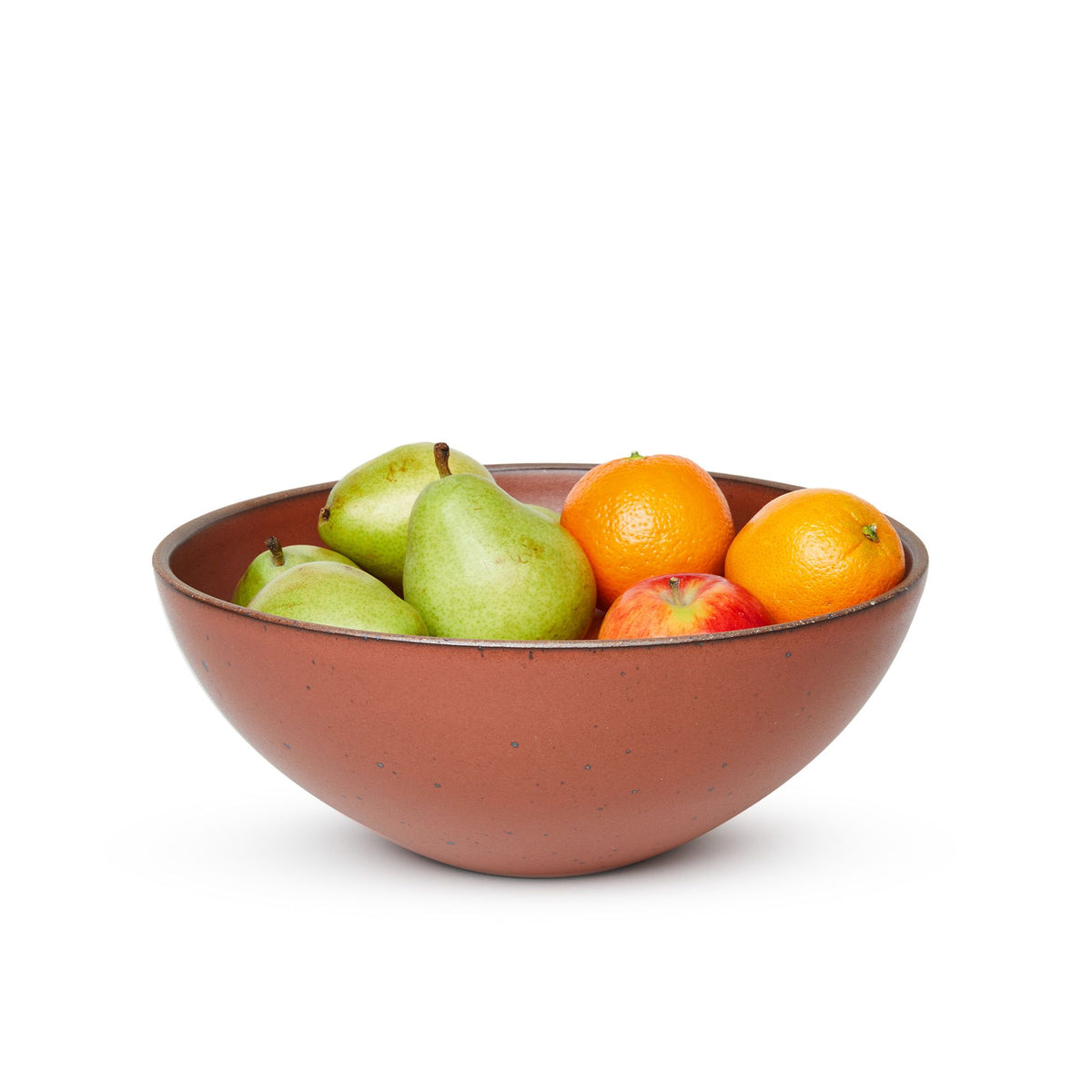 A large ceramic mixing bowl in a cool burnt terracotta color featuring iron speckles and an unglazed rim filled with pears, oranges and apples
