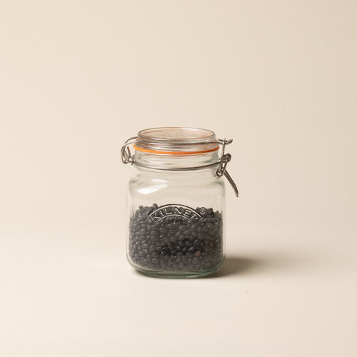A short storage glass square jar, filled with beans, topped with a lid with a rubber seal and steel clip closure.