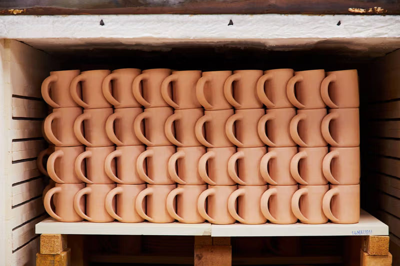 Rows of unglazed ceramic mugs neatly stacked inside a kiln, ready for firing.