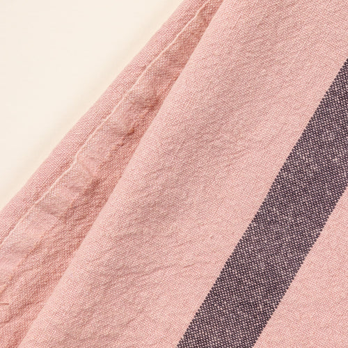 A close up of a folded linen towel in a salmon color with a plum stripe in the middle