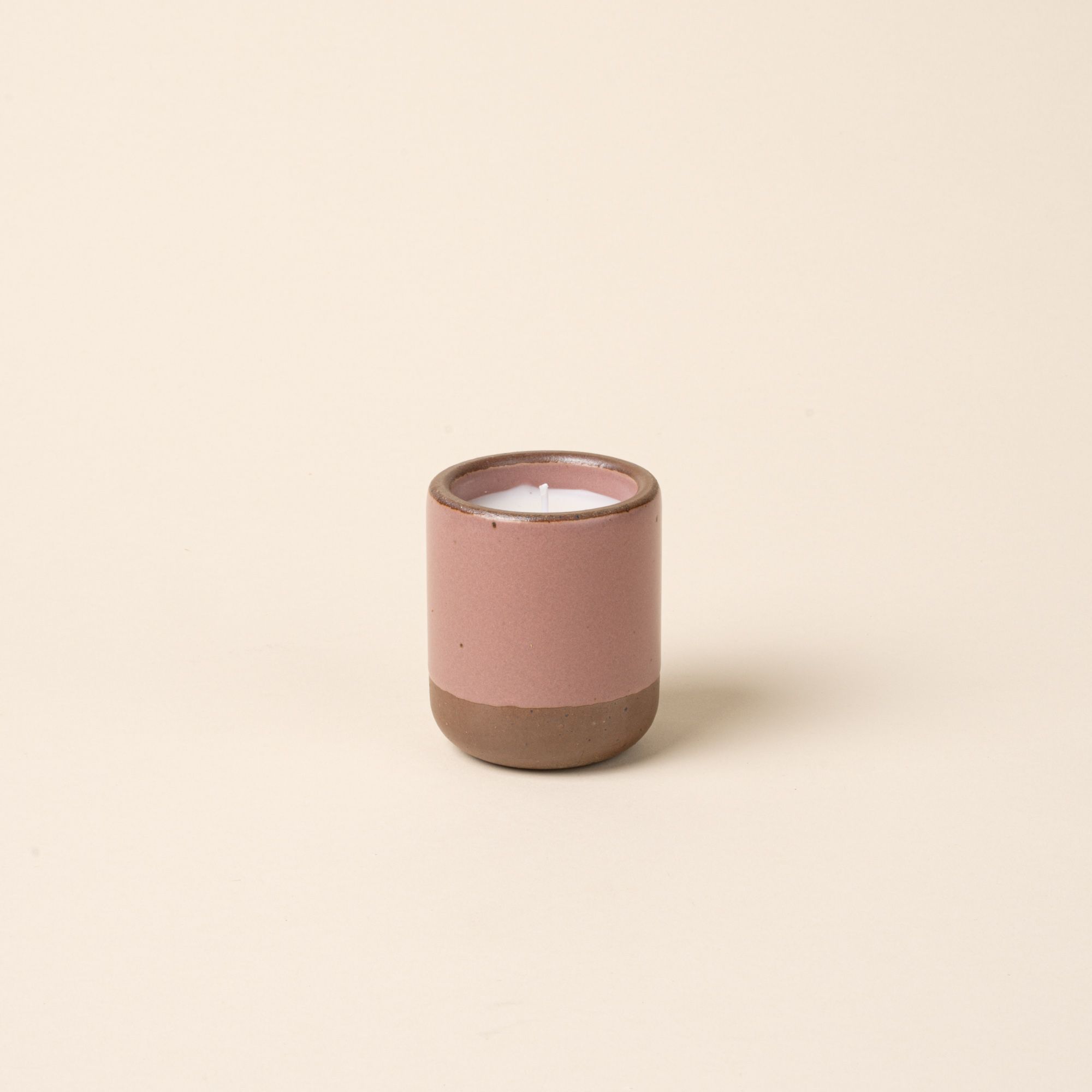 Small ceramic vessel in a soft mauve pink color with poured candle inside.