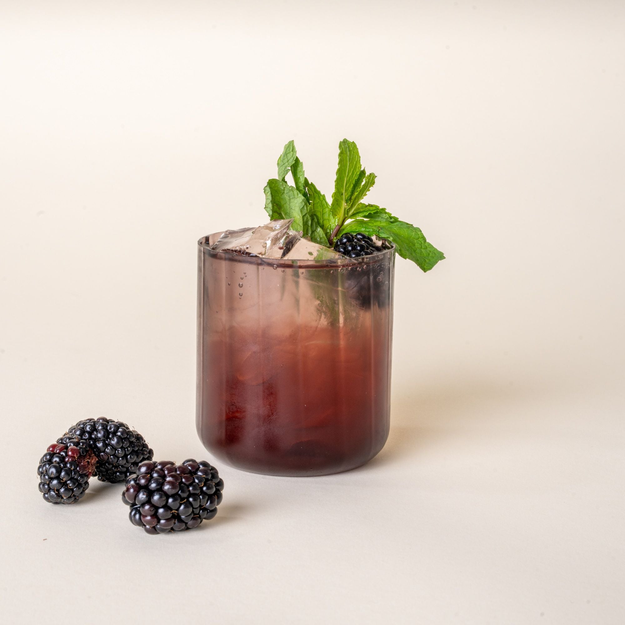 A cocktail in a fluted walled tumbler in a grey purple color, with raspberries nearby.