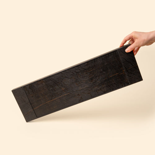 Hand holds out a narrow rectangle of ebonized oak wood with a vertical groove at either end