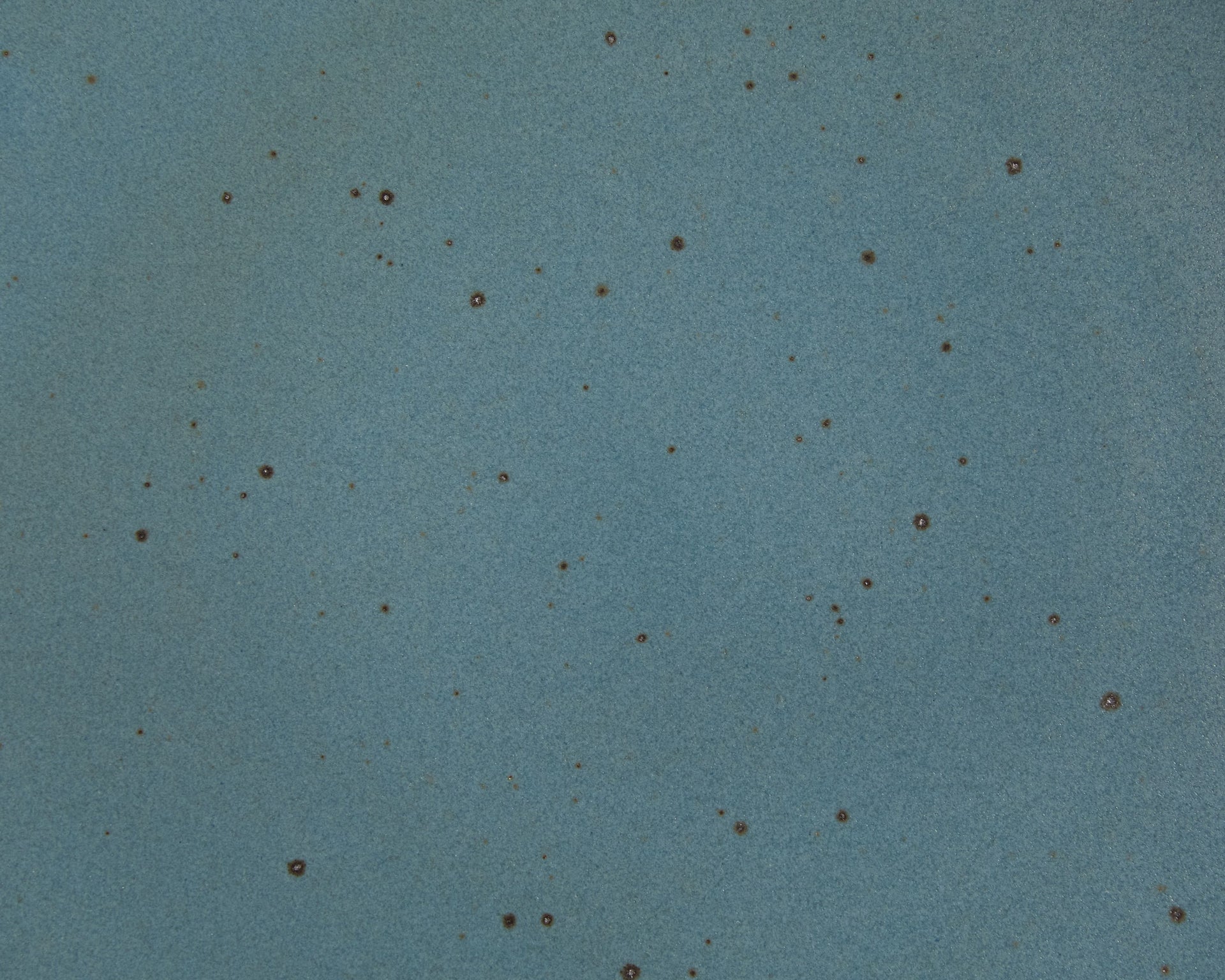 A closeup of a ceramic plate in a turquoise color with iron speckles throughout