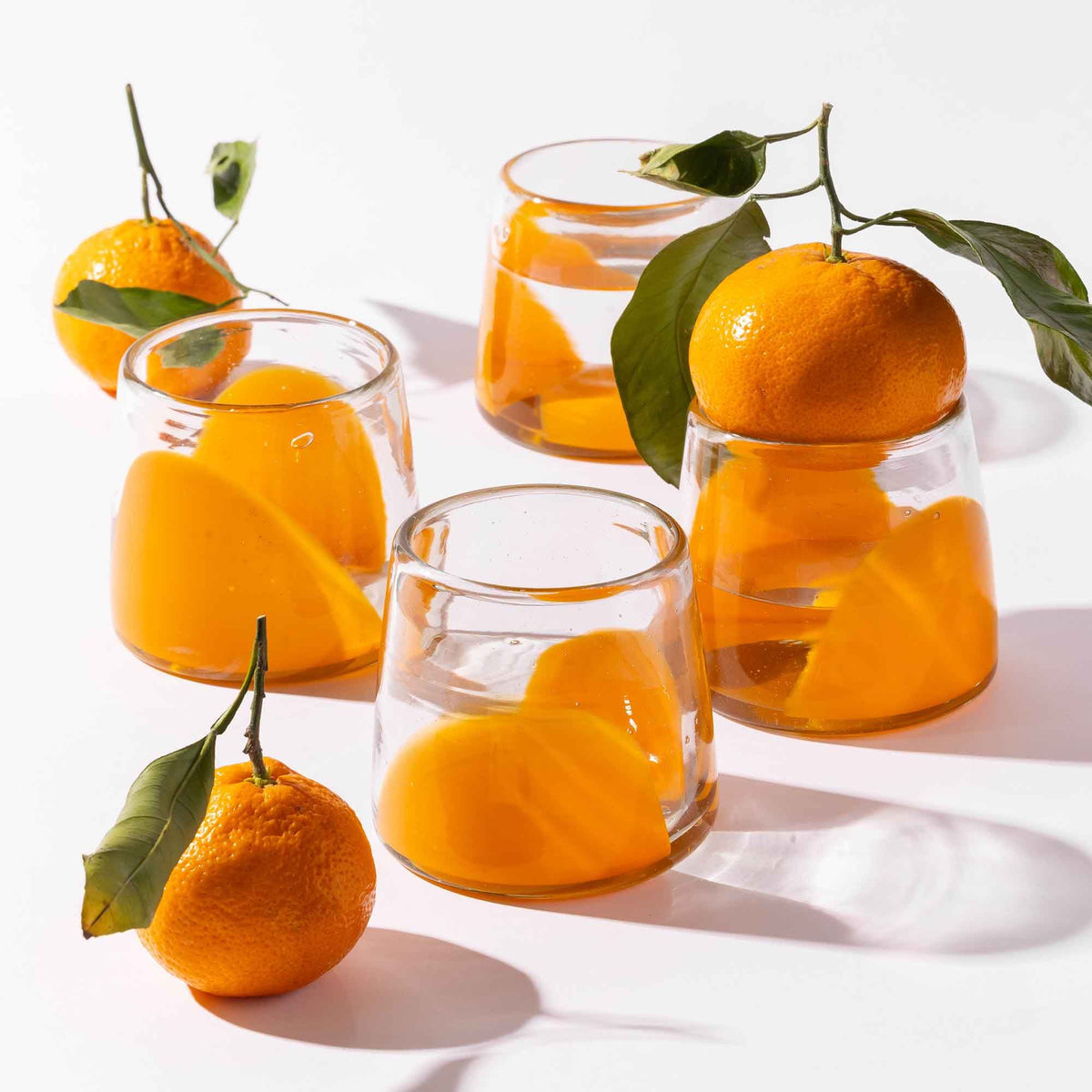 Four short clear glasses with orange arch bases, styled with clementines.