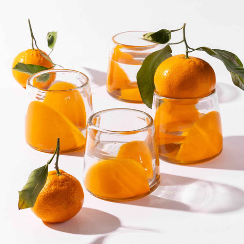 Four short clear glasses with orange arch bases, styled with clementines.