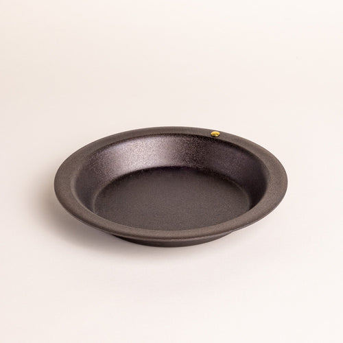 A small simple iron pie dish with a wide rim and shallow body