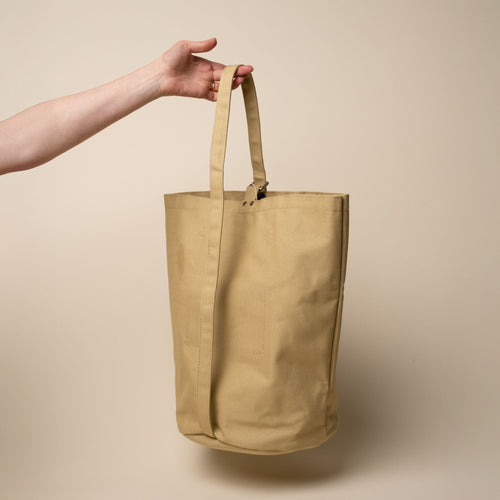 A hand holds up a large simple canvas bucket tote by the top handle
