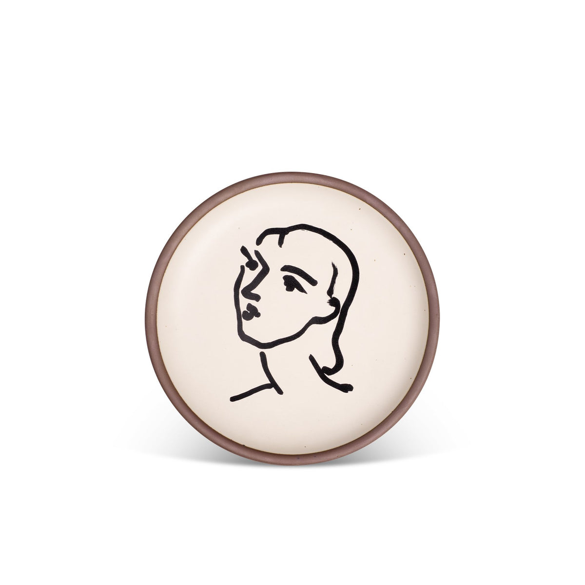 A ceramic plate featuring a decal of the artwork, Nadia aux cheveux lisses, by Henri Matisse. A minimalist black ink decal of a woman's face and neck in profile, facing left, in an abstract, expressive style centered on an off-white ceramic plate with an unglazed rim.